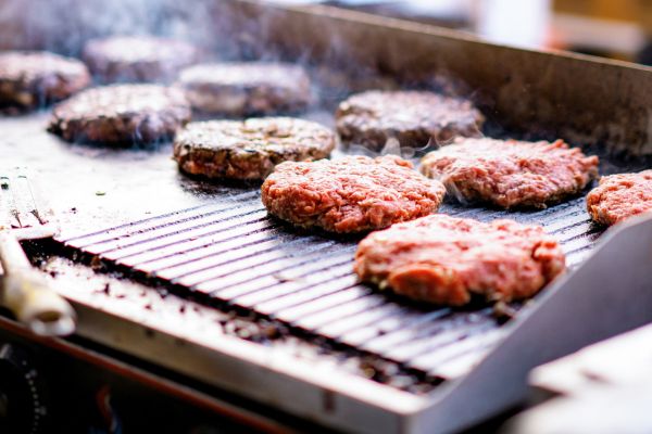 Beef patties grilling on a BBQ with smoke rising.