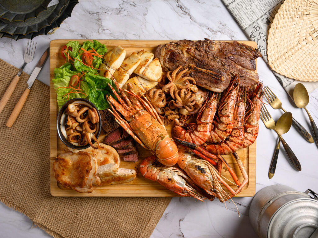 Grilled seafood and meats including shrimp, lobster, steak, and chicken on a wooden platter.